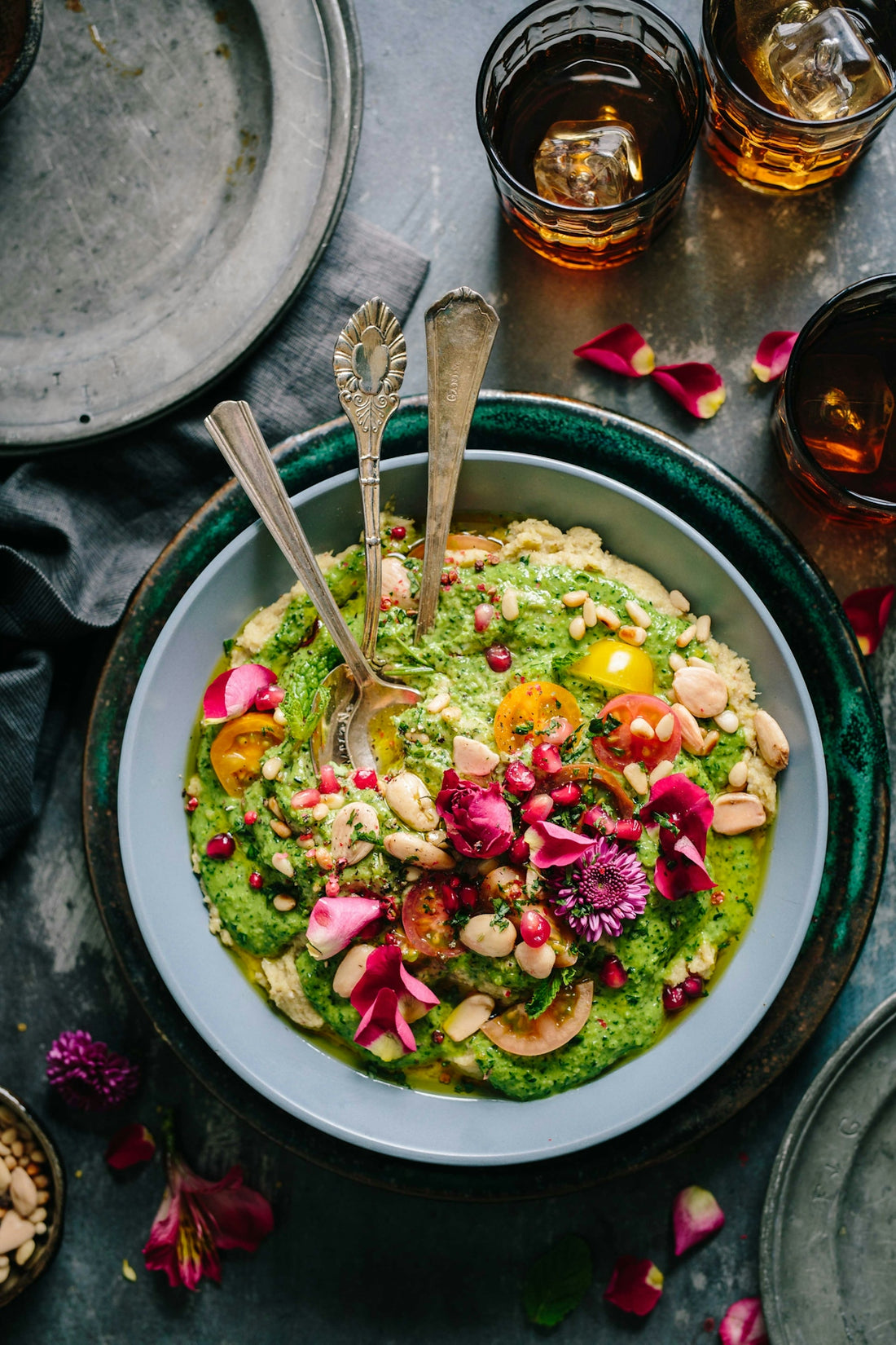 Hummus topped with green herb sauce, cherry tomatoes, pomegranate seeds, and edible flowers
